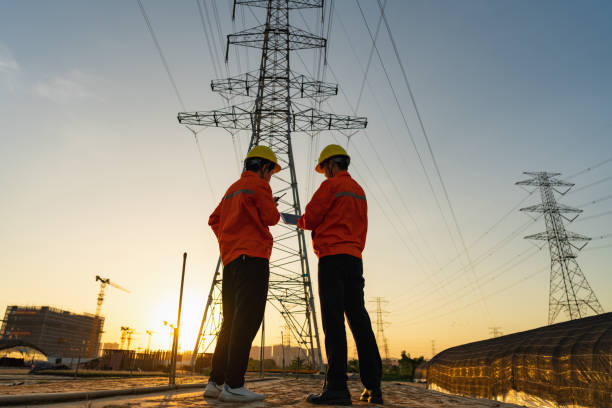Two electric workers using tablet computer at sunset stock photo