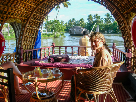 Alappuzha, Kerala, India - nov 14, 2005: a traveler, comfortably seated in a small lounge on the houseboat, enjoys a cruise in the Backwaters of Kerala