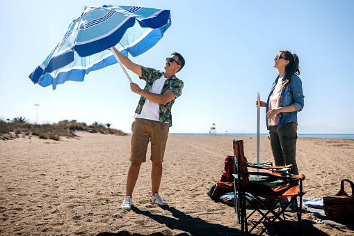 Couple setting up parasol for their camping spot on the beach