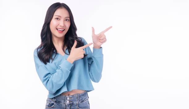 istock Cheerful excited asian woman use finger pointing to side with product or empty copy space standing over isolated white background. Model young girl laughing promotion. Advertisement presenting concept 1437215545