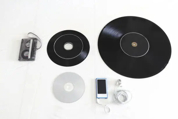 Tape cassette, 45 rpm record, 33 rpm vinyl record and music CD on a white background.