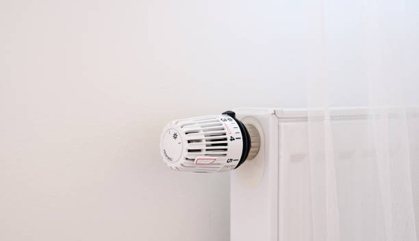 istock Thermostat close-up. Battery temperature controller. White heater with thermostat on the wall in modern apartment. Heating service cost concept, utility price increase. Temperature control valve. 1437218250