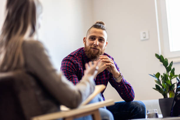 psychologin spricht während der sitzung mit einem jungen mann. - mental health professional therapy patient psychiatrist stock-fotos und bilder