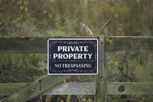 An art deco inspired black sign with white writing stating private property no trespassing on a aged wooden fence with two feathers placed on top