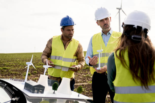 istock Three caucasian and latin engineers standing on wind turbine field and discussing lively over plastic models 1437227463