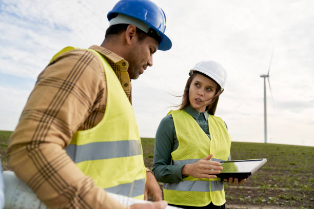 istock Caucasian and latin engineers standing on wind turbine field with a sample solar panel and discussing 1437228663