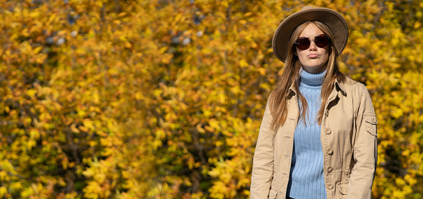 Woman in a coat with a hat in the autumn park. Background of yellow foliage in nature. Banner