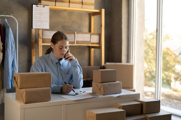 istock Small business owners, startup and e-commerce concept. Smiling friendly young woman talking with customer over phone, while packing orders for shipping, online clothes store 1437229084