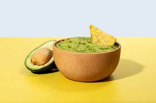 Mexican guacamole with nacho chip on yellow background