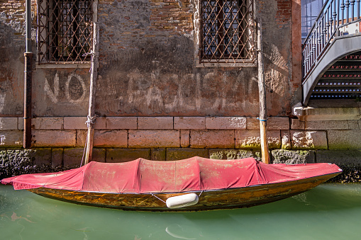 Venice, Italy - October 7th 2022: Small motorboat covered with a tarpaulin moored at the side of a canal in the old and famous Italian city Venice