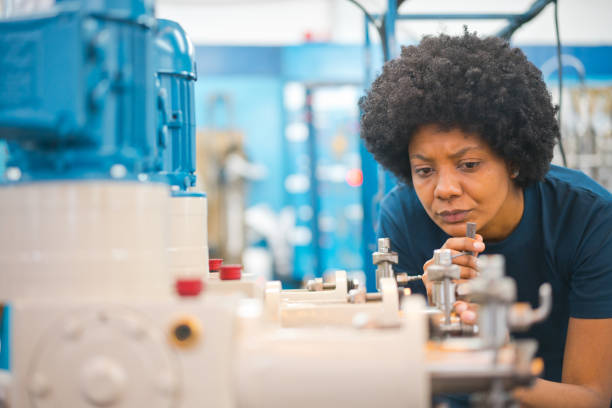 female blue-collar worker analyzing machinery in factory - african descent factory accuracy analyzing imagens e fotografias de stock