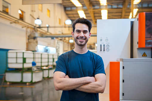 Portrait of happy male blue-collar worker standing with arms crossed in factory
