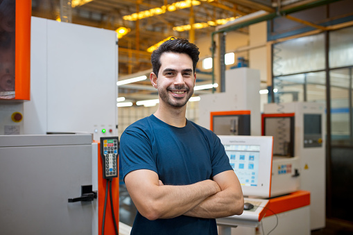 Portrait of smiling young male engineer standing with arms crossed in factory