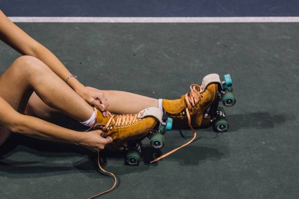 young woman lacing up roller skates young woman lacing up roller skates on court at night roller skating stock pictures, royalty-free photos & images