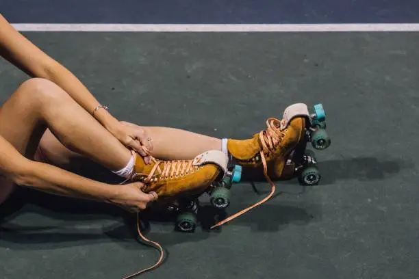 young woman lacing up roller skates on court at night