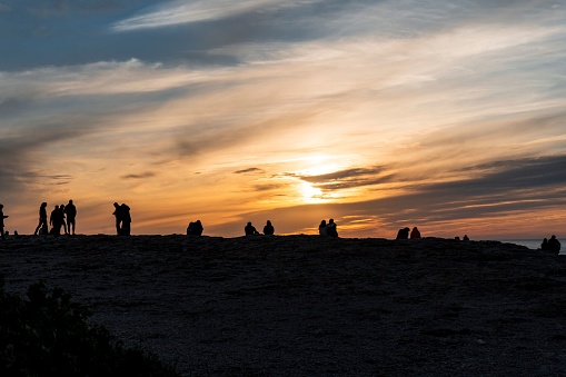 People sihouettes on cliff in front of colorful Sunset over Atlantic Ocean with yellow and orange gradient