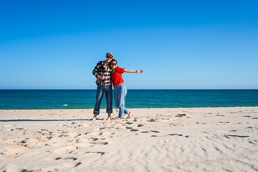 Tourist couple standing on wide open white beach under blue sky with ocean in the back
