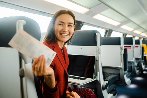 Beautiful Asian businesswoman on a journey traveling by a train and showing her ticket
