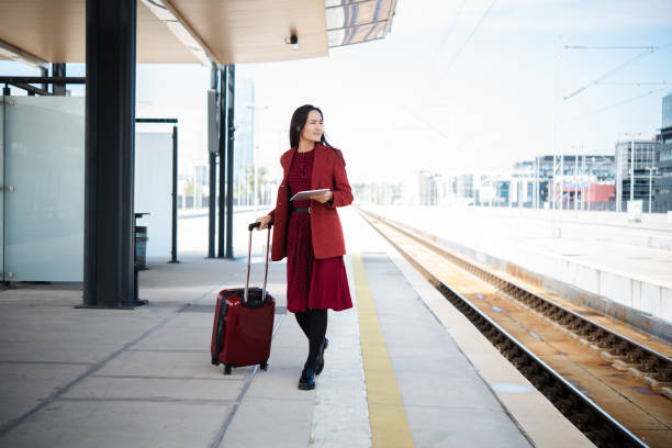Beautiful Asian businesswoman on a journey waiting at the train station and using a digital tablet