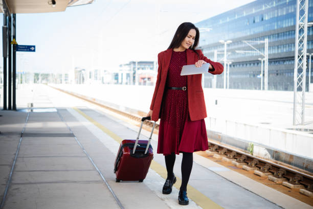 Beautiful Asian businesswoman on a journey waiting at the train station and using a digital tablet