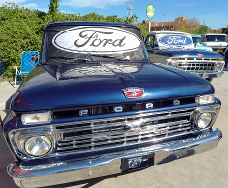 Avellaneda, Argentina – May 08, 2022: Ford oval logo and brand on the windshield of an old blue F100 utility pickup truck 1966. Front View. Expo Fierros 2022 classic car show