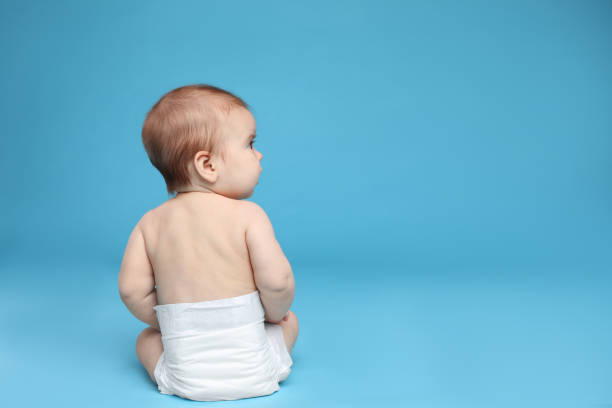 istock Cute little baby in diaper sitting on light blue background. Space for text 1437239983