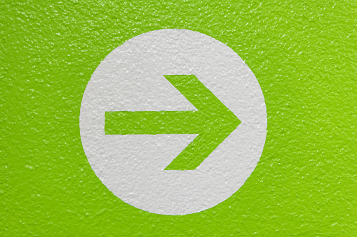 An arrow on a white circle isolated on a green wall showing the direction