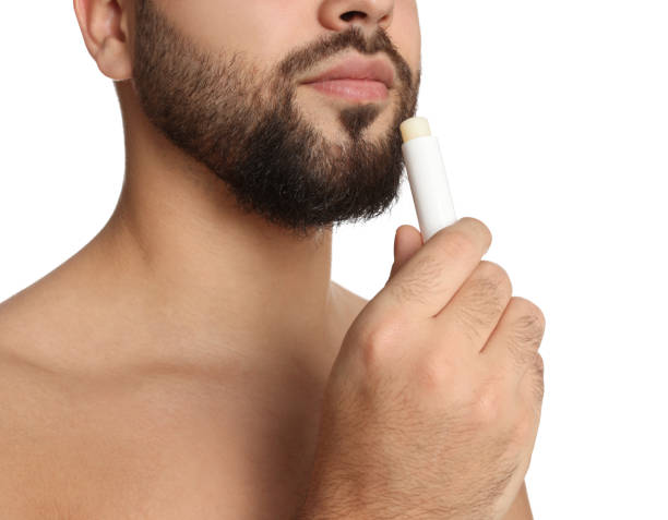 istock Young man applying lip balm on white background, closeup 1437240951
