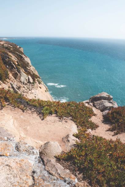 istock Vertical shot from a cliff top to rocky cliffs with grass by the tranquil sea 1437241661