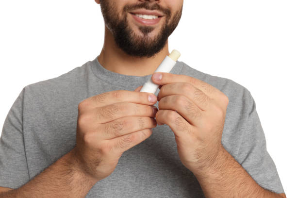 istock Young man with lip balm on white background, closeup 1437241662