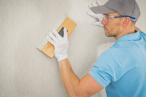 A caucasian worker in modern vinyl wallpaper using a squeegee