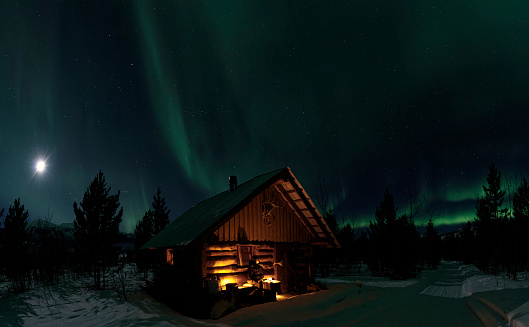 Winter night scene of log cabin with full moon and northern lights