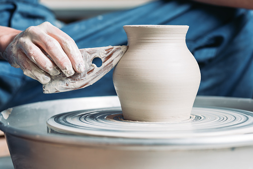 Woman hands working with tool on pottery wheel and making a pot.