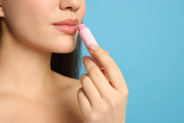istock Young woman applying lip balm on turquoise background, closeup. Space for text 1437244452
