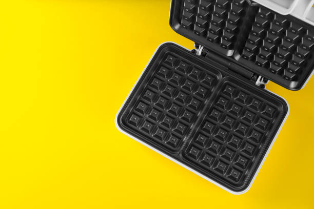 istock Open electric waffle maker on yellow background, top view. Space for text 1437245066