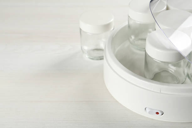 istock Modern yogurt maker with empty jars on white wooden table, closeup. Space for text 1437245720