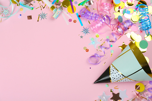 Colorful serpentine streamers, party hat, horn and confetti on pink background, flat lay. Space for text