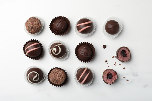 Different delicious chocolate truffles on white marble table, flat lay