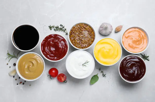 Photo of Many different sauces on light grey table, flat lay