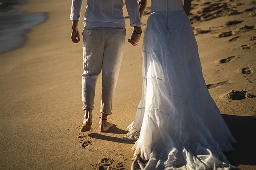 A low angle shot of the bride and the groom walking through the wet sand at the beach