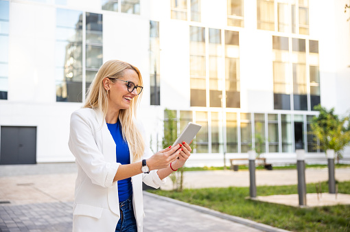 Side-view of modern Caucasian businesswoman using digital tablet in front of the corporate building