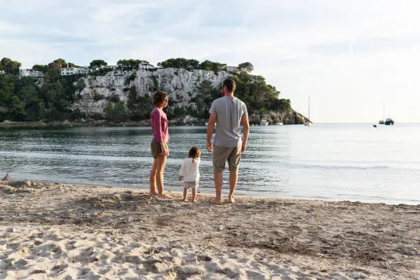 Photo of Mother, father and their little daughter enjoying the sunset at a nice sand beach called cala Galdana located in Minorca, spain.