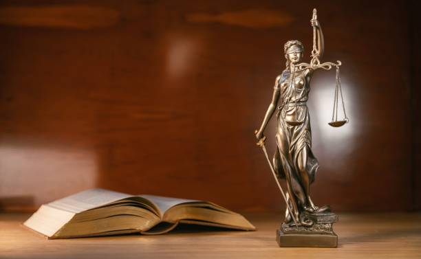 istock Statue of lady justice and a book on a brown background copy space for text 1437248559