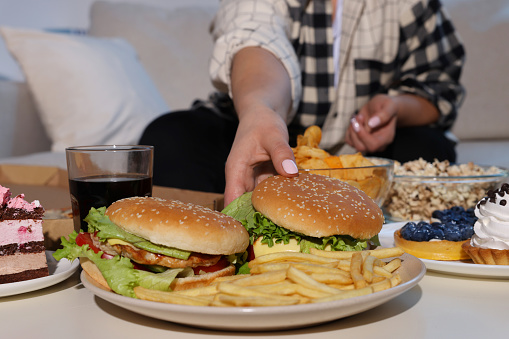 Mujer con sobrepeso tomando hamburguesa en casa, primer plano photo