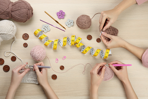 Women crocheting with threads at wooden table, top view