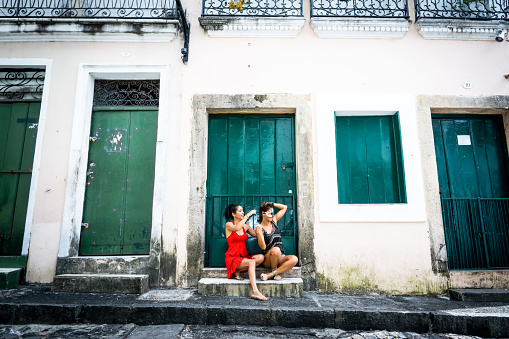 Portrait of two beautiful and happy girls sitting against a green colored door. City girls far from the capital. They handle a carnival mask.