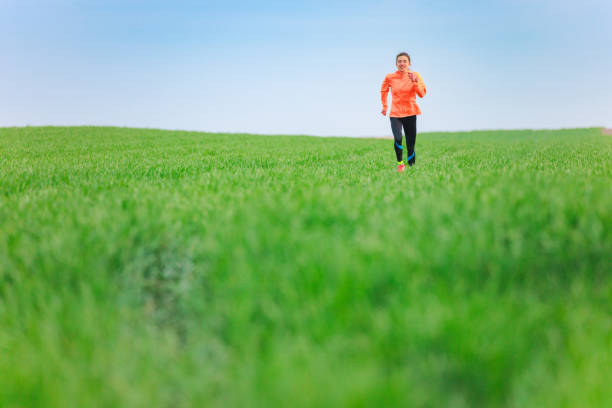 Young woman running through the field with green grass under the blue sky, cross-country running