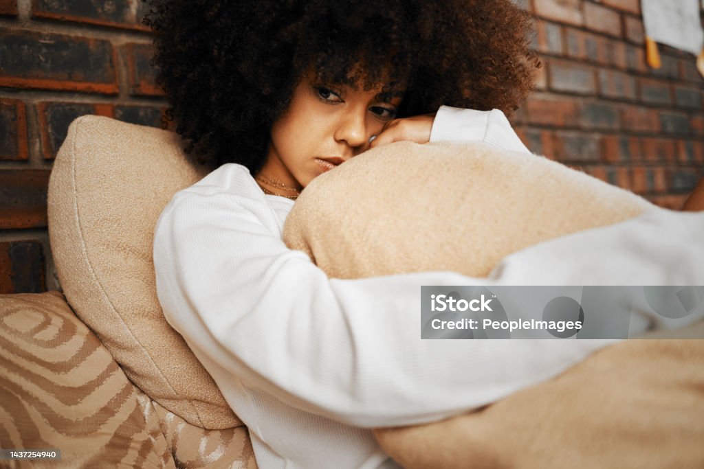 Sad, depressed and lonely black woman with mental health problems hugging a pillow at home. Portrait of a African afro female in depression, stress and anxiety feeling unhappy living alone in a house Sadness Stock Photo