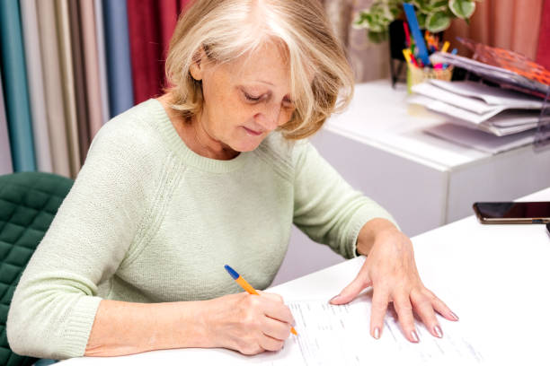 istock Senior woman working with document at fabric store indoor. Designer writing at table. Fabric and furniture shop 1437254960