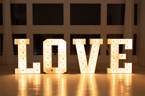 Glowing large letters. Wedding decor. Illuminated Love sign in large letters near window. Love big white letters with led retro bulbs glowing. Word LOVE with a big letters. Inscription is love.